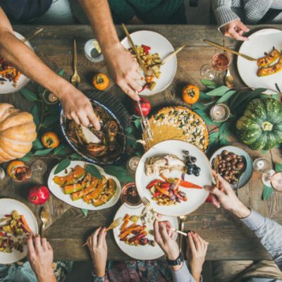 Traditional Thanksgiving or Friendsgiving holiday celebration party. Flat-lay of friends or family feasting at Thanksgiving Day festive table with turkey, pumpkin pie, roasted seasonal vegetables and fruit, top view.